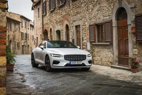Weißer Polestar 1 Plug-in-Hybrid-Coupé auf nasser Kopfsteinpflasterstraße vor historischen Gebäuden