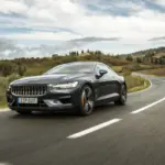 Polestar 1 fährt dynamisch auf einer kurvigen Landstraße bei bewölktem Himmel.