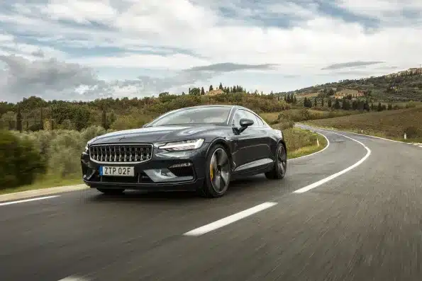 Polestar 1 fährt dynamisch auf einer kurvigen Landstraße bei bewölktem Himmel.