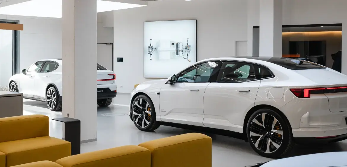 Mehrere weiße Polestar Fahrzeuge in einem modernen Showroom mit großen Fenstern und gelben Sitzmöbeln.