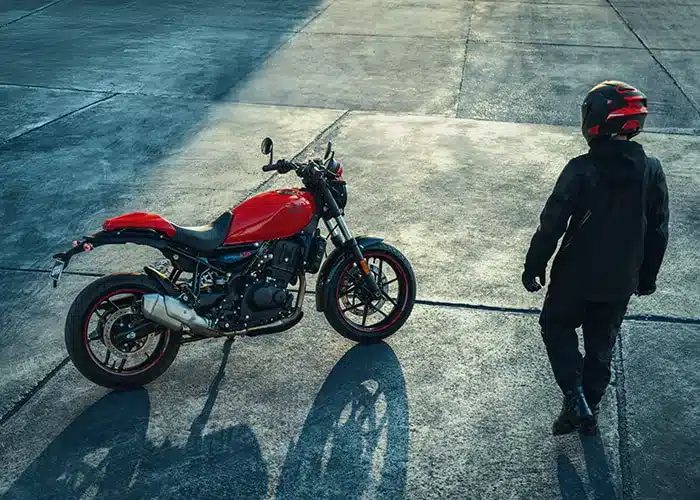 Royal Enfield Guerrilla 450 in rot steht auf Asphalt mit Fahrer in Motorradkleidung daneben.