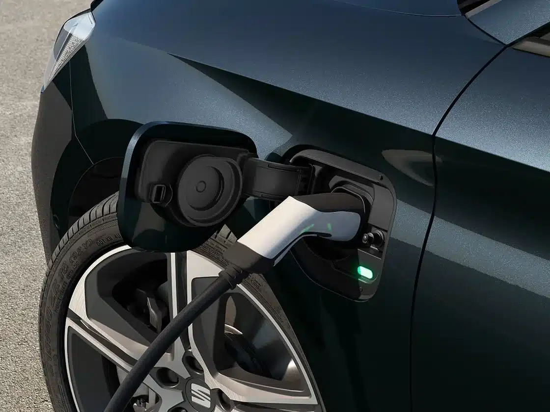 SEAT Leon e-HYBRID lädt an einer Ladestation, Nahaufnahme des Ladeanschlusses und Rads.