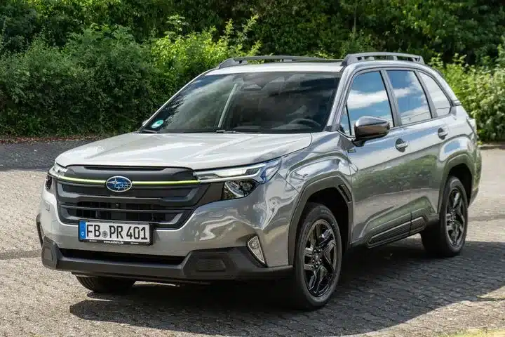Subaru Forester e-BOXER, silberfarben, Modell 2024, steht auf einem gepflasterten Parkplatz vor grüner Vegetation.
