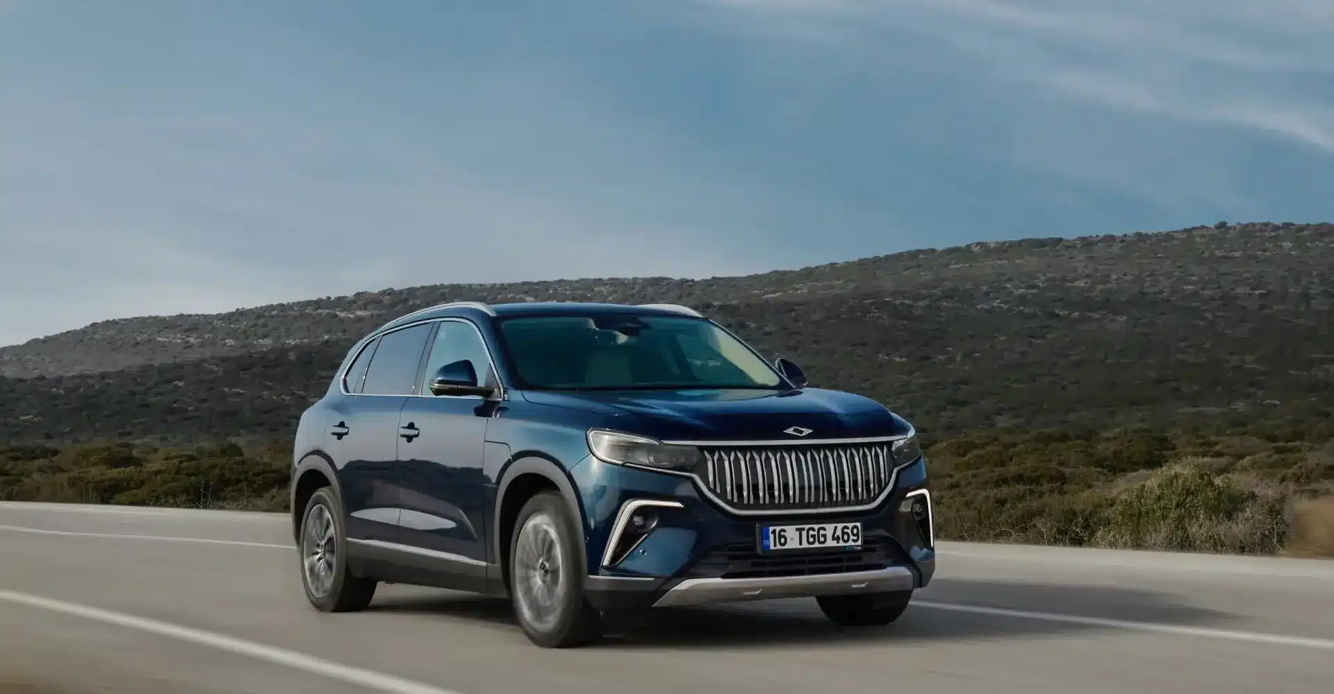 Der Togg T10X, ein elektrischer SUV, fährt auf einer Landstraße vor hügeliger Landschaft.
