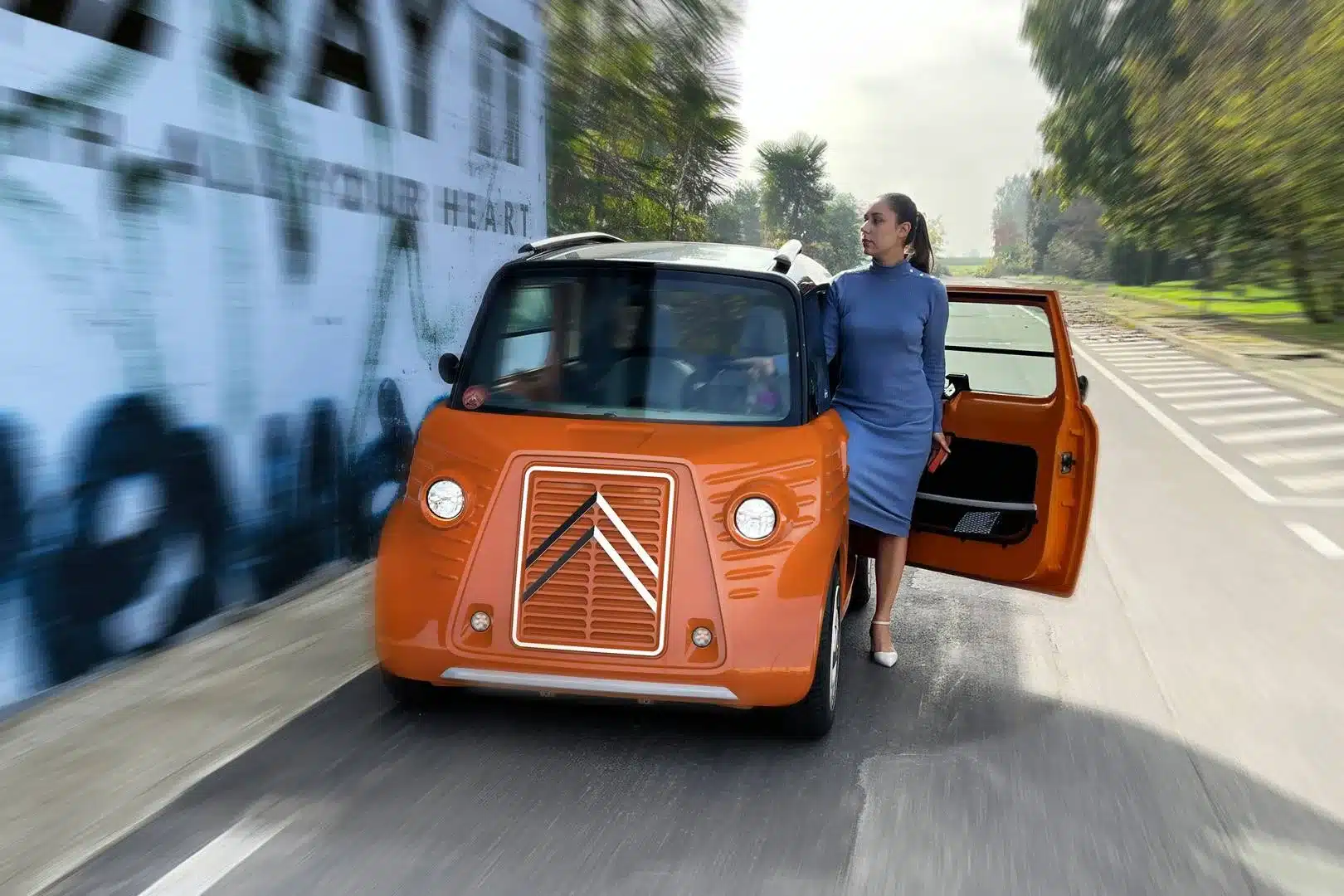 Orangefarbener Citroën Type-Ami von Caselani im Stil des HY mit einer Frau an der geöffneten Tür auf einer Straße.