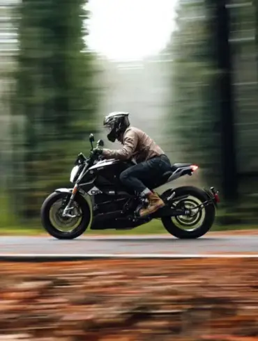 Fahrer auf einer Zero SR/F fährt dynamisch durch einen Wald auf einer Landstraße.