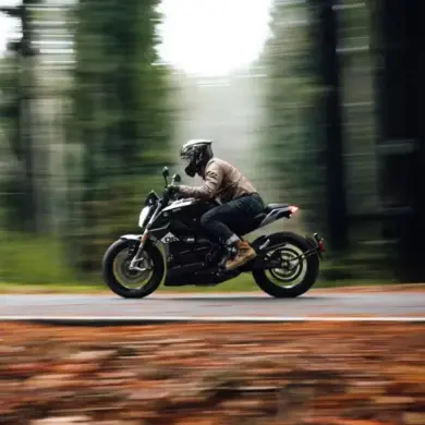 Fahrer auf einer Zero SR/F fährt dynamisch durch einen Wald auf einer Landstraße.