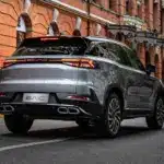BAIC Beijing X75 silberfarben, Heckansicht auf einer breiten Stadtstraße vor historischer Backstein-Architektur.
