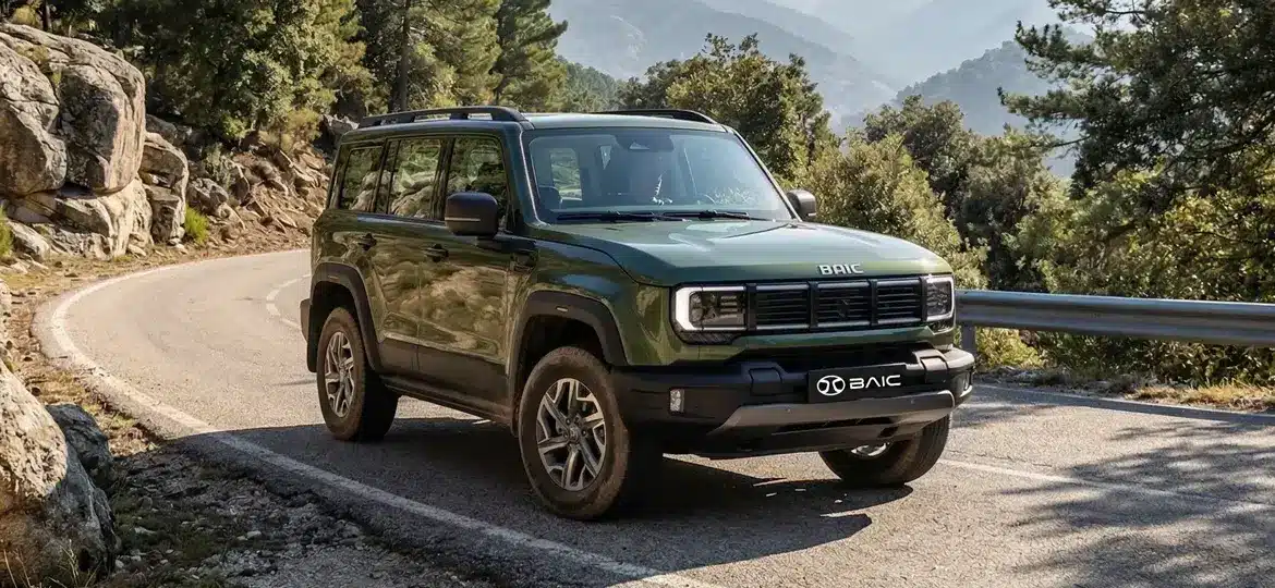 Grüner BAIC BJ40 D Pro SUV fährt auf einer kurvigen Bergstraße, umgeben von Felsen und Wald.