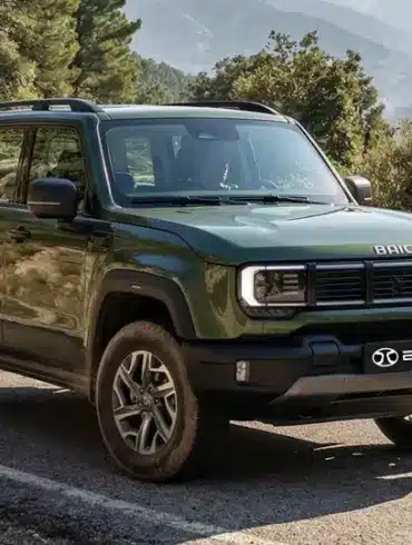 Grüner BAIC BJ40 D Pro SUV fährt auf einer kurvigen Bergstraße, umgeben von Felsen und Wald.