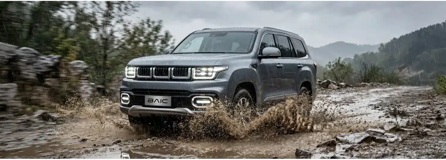 BAIC BJ60 Flagship fährt bei Regen durch Matsch auf einer unbefestigten Straße im Gelände.