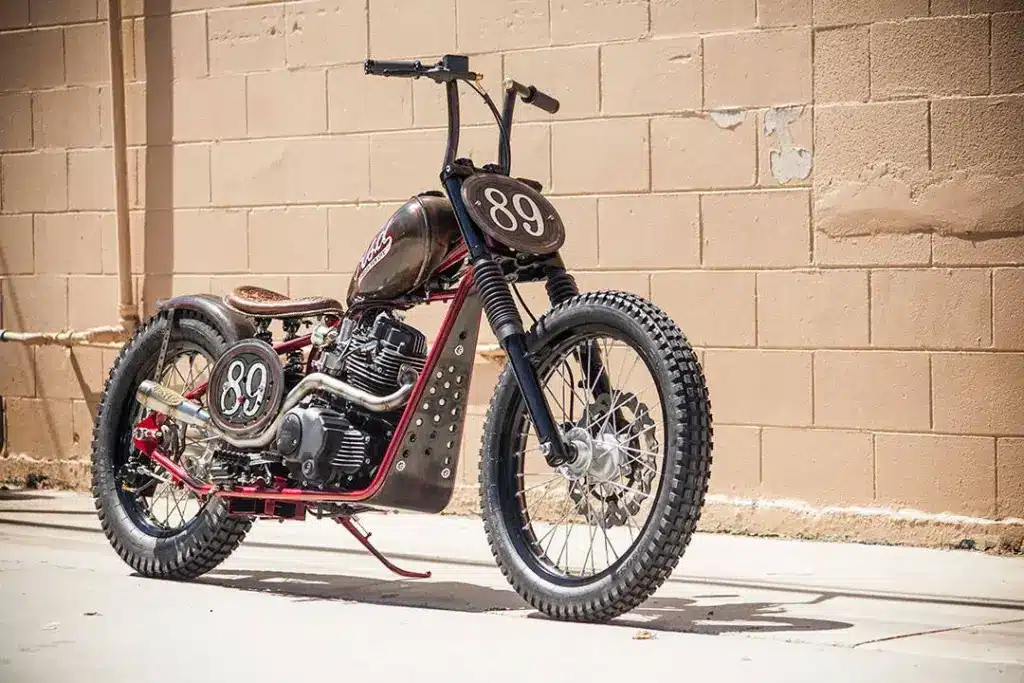 Cleveland CycleWerks Heist Chopper mit braunem Tank, Starrrahmen und Startnummer 89, seitlich vor einer Mauer fotografiert