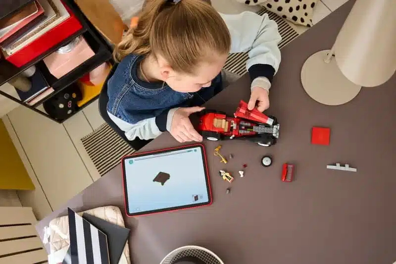 Kind baut das LEGO Set 43277 Cruella de Vils Auto auf einem Tisch mit Tablet und Werkzeugen