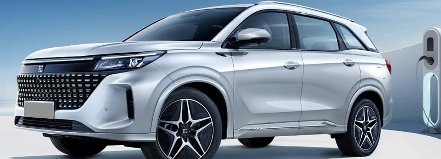 DFSK Fengon E5 PHEV in Silber steht an einer Ladesäule vor blauem Himmel.
