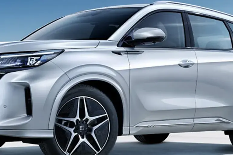 DFSK Fengon E5 PHEV in Silber steht an einer Ladesäule vor blauem Himmel.