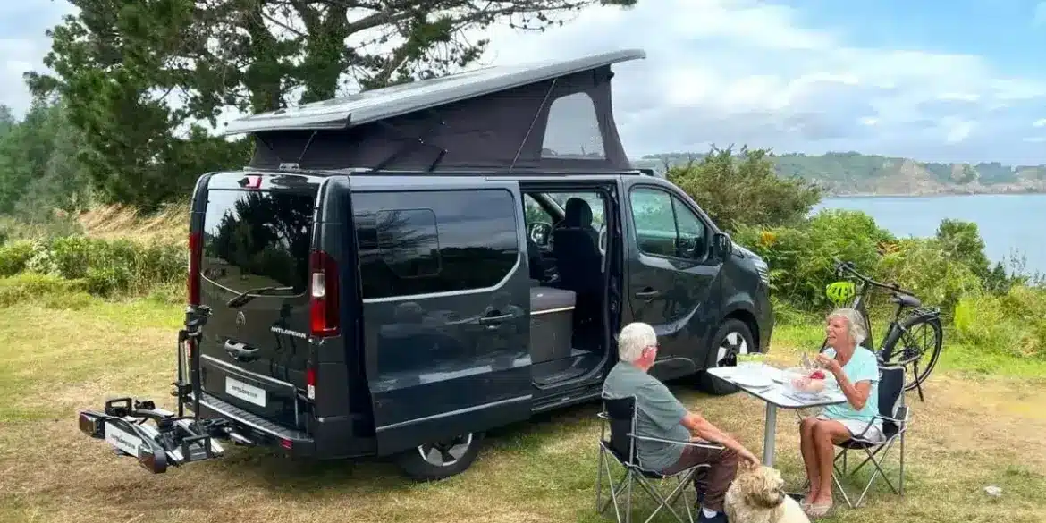 Flex PLUS Campervan mit geöffnetem Aufstelldach, sitzendem Paar und Hund an einem Tisch in der Natur