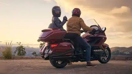Zwei Personen fahren auf einer roten Honda GL1800 Gold Wing Tour bei Sonnenuntergang.