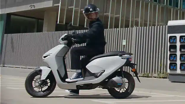 Seitenansicht des Honda CUV e: Elektrorollers mit Fahrer vor moderner Architektur.