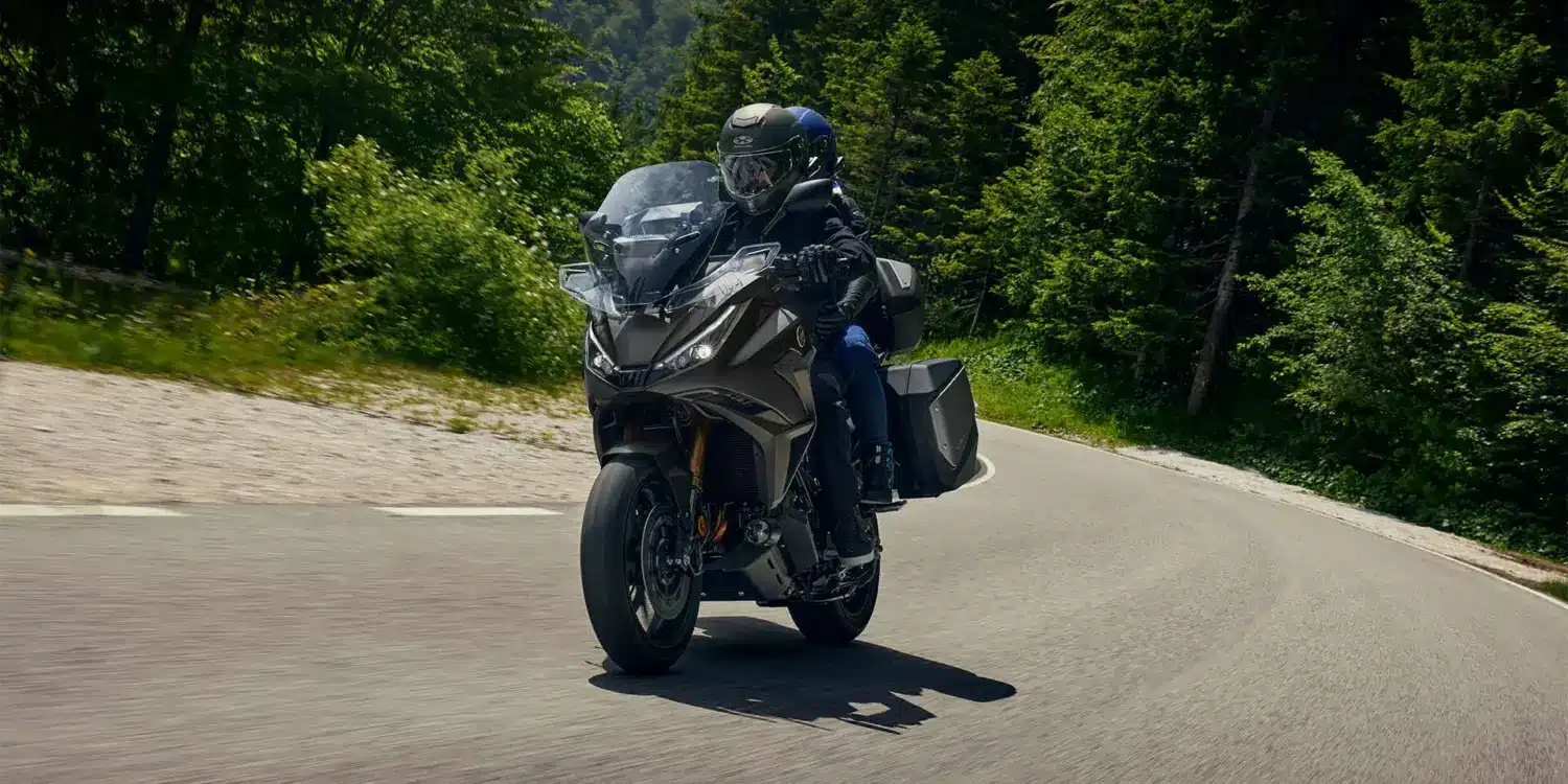 Honda NT1100 2026 mit zwei Fahrern auf Landstraße, Seitenkoffer und Windschutz gut sichtbar.
