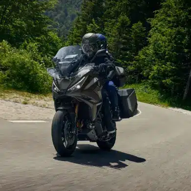 Honda NT1100 2026 mit zwei Fahrern auf Landstraße, Seitenkoffer und Windschutz gut sichtbar.