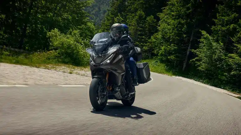 Honda NT1100 2026 mit zwei Fahrern auf Landstraße, Seitenkoffer und Windschutz gut sichtbar.