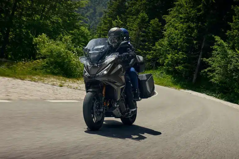 Honda NT1100 2026 mit zwei Fahrern auf Landstraße, Seitenkoffer und Windschutz gut sichtbar.