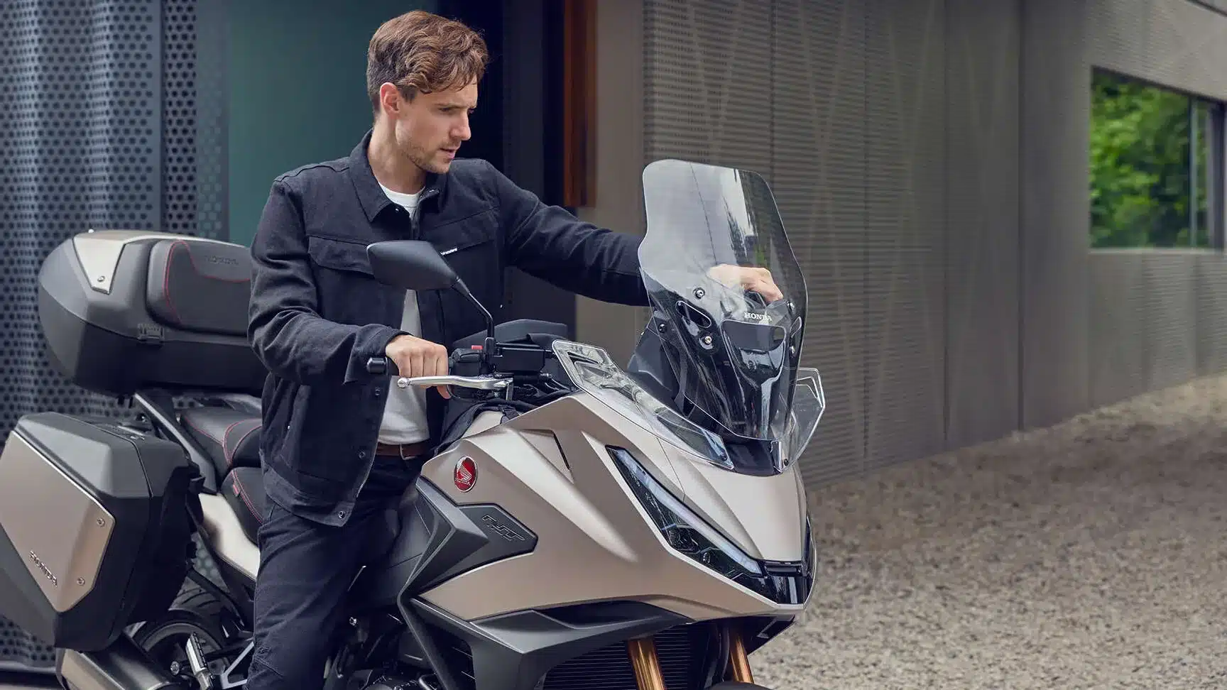 Fahrer mit Honda NT1100 2026 vor modernem Gebäude, Fokus auf Verkleidung, Windschutz und Koffersystem.
