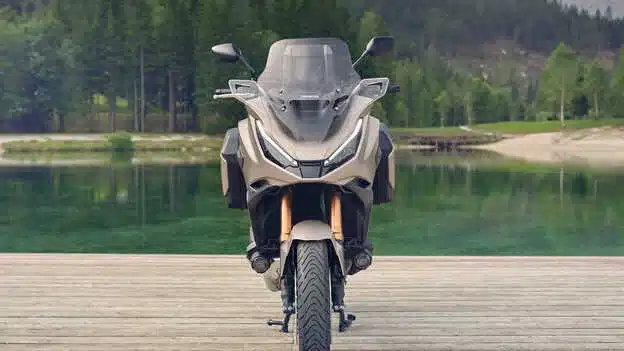Honda NT1100 2026 von vorne, geparkt auf Holzsteg am See vor bewaldeter Landschaft.
