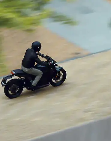 Eine Person fährt die Honda WN7, ein elektrisches Naked Bike, auf einer Straße, seitliche Ansicht