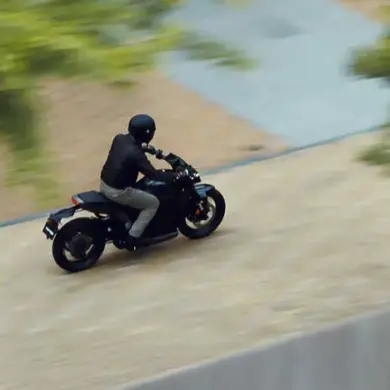 Eine Person fährt die Honda WN7, ein elektrisches Naked Bike, auf einer Straße, seitliche Ansicht