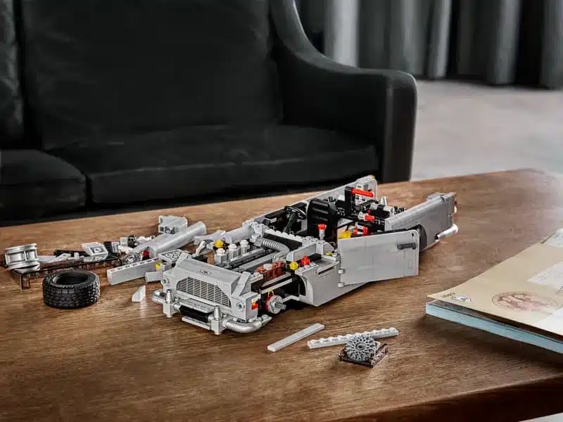 Halb aufgebautes LEGO Modell des James Bond Aston Martin DB5 auf einem Holztisch, umgeben von Einzelteilen.
