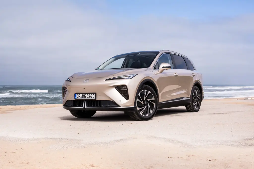 Beiger MG IM6 Elektro-SUV steht an einem Strand mit Meer im Hintergrund.
