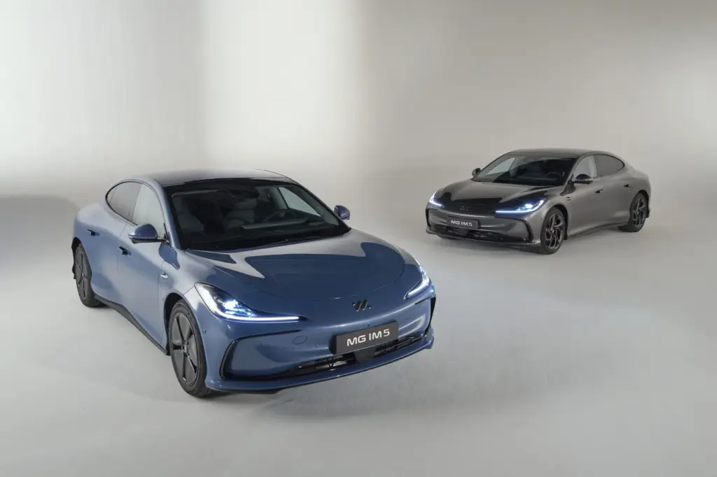 Zwei MG IM5 Elektroautos in einem hellen Studio, vorne in Blau, hinten in Schwarz.