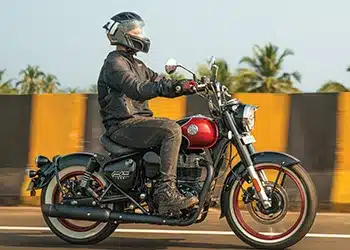 Motorradfahrer fährt eine Royal Enfield Goan Classic 350 im Bobber-Stil, rote Lackierung, Seitenansicht.