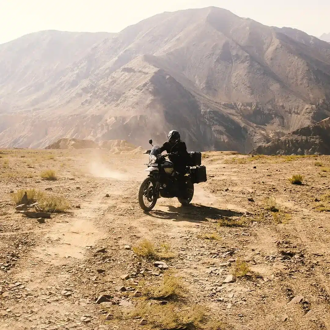 Abenteuermotorrad Royal Enfield Himalayan 450 fährt auf unbefestigtem Weg durch bergige Landschaft.