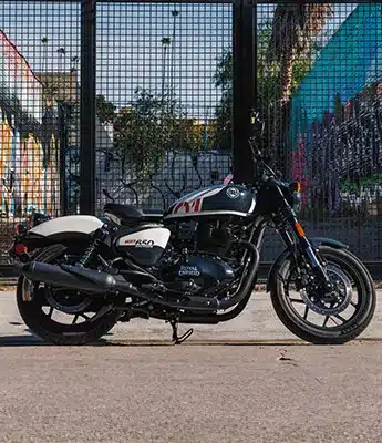 Seitenansicht der Royal Enfield Shotgun 650 vor einem urbanen Hintergrund mit Graffiti.