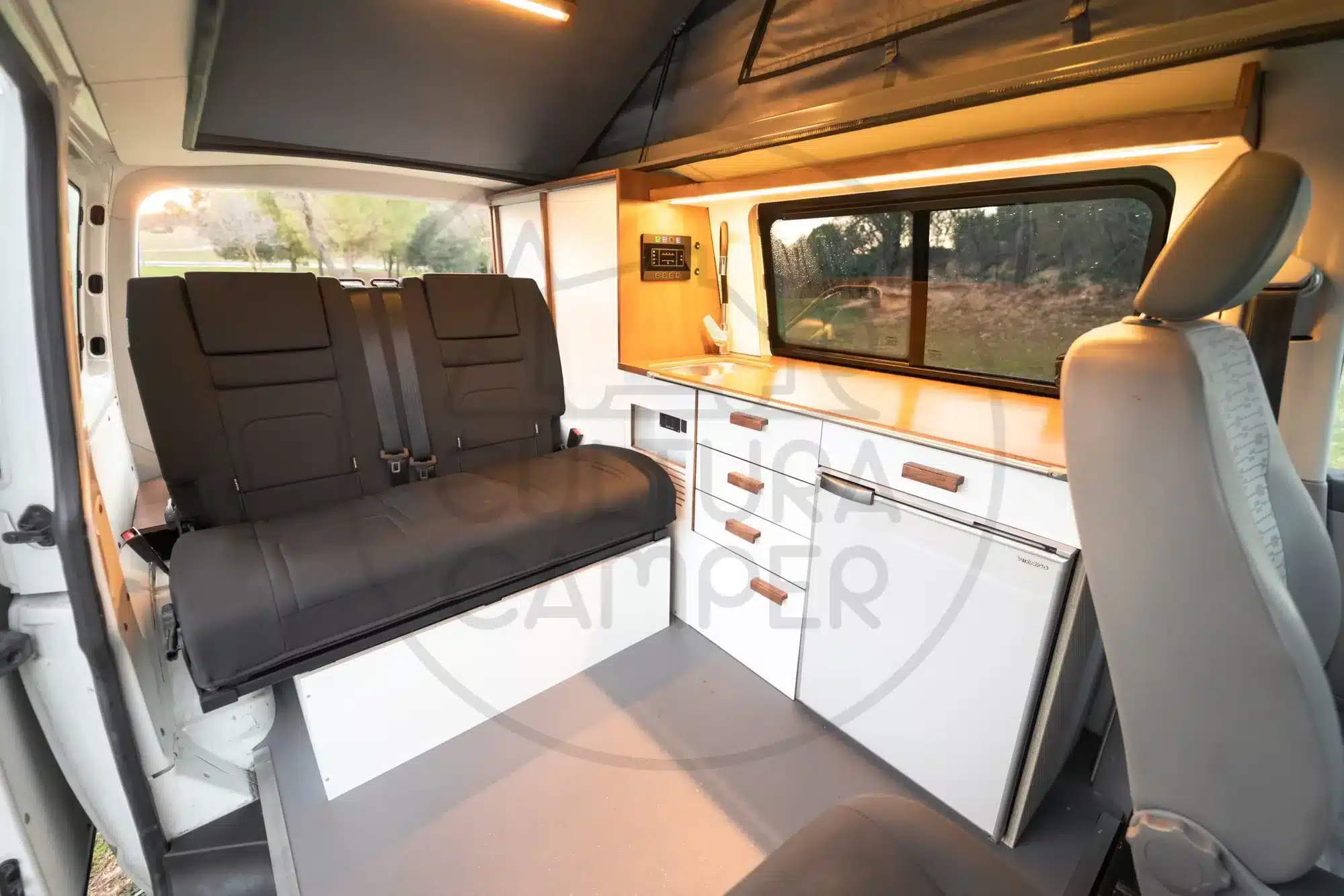 Wohnbereich eines Volkswagen T6 Campervans mit Sitzbank, Küchenzeile und geöffnetem Aufstelldach