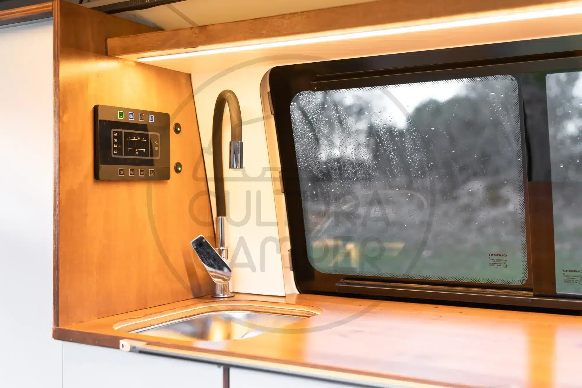 Kompakte Küchenzeile mit Edelstahleinbauspüle, Wasserhahn und Steuerpanel im Innenraum eines VW T6 Campers aus Spanien.