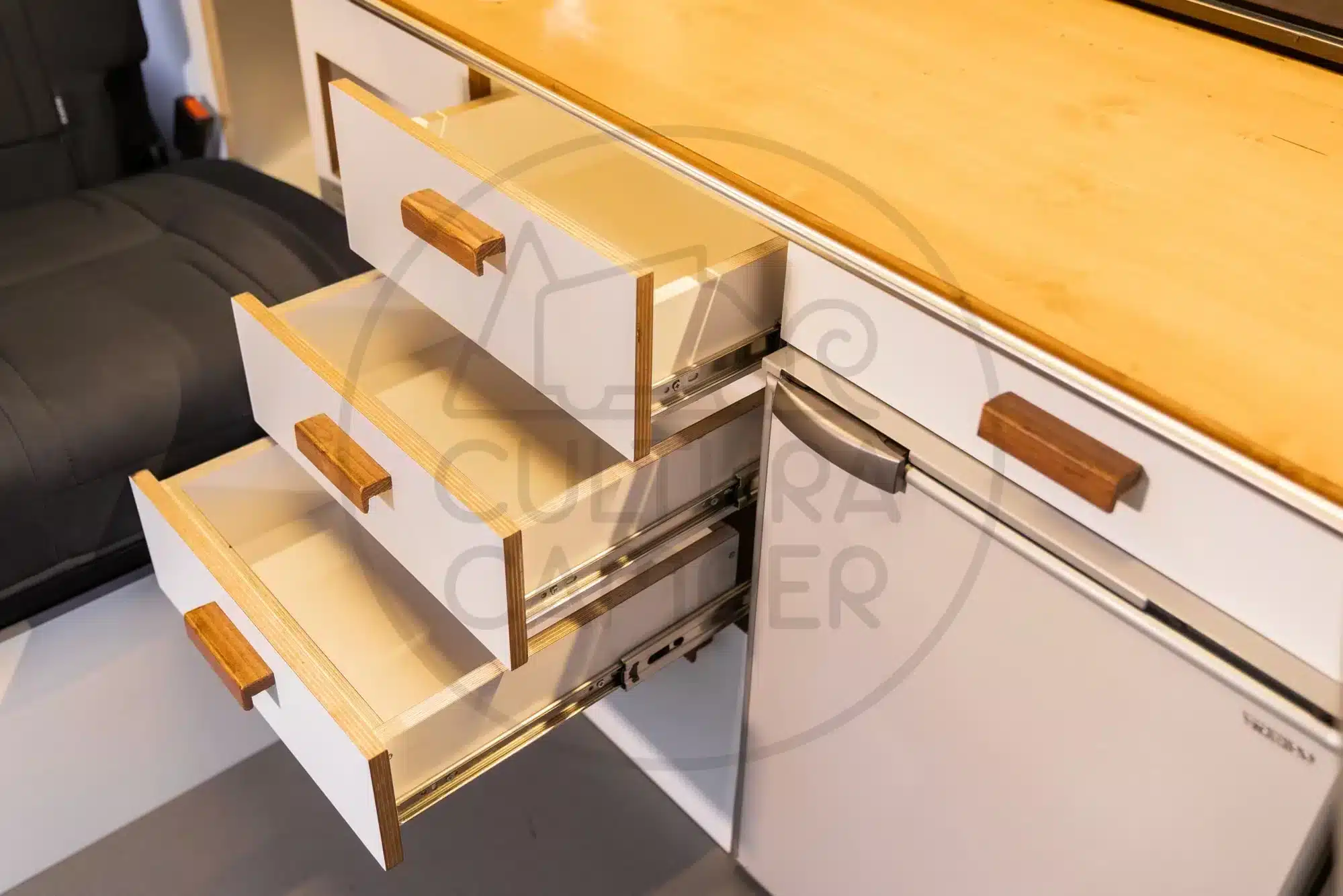 Offene Schubladen und Kühlschrank im Küchenblock eines Volkswagen T6 Campervans, Nahaufnahme.