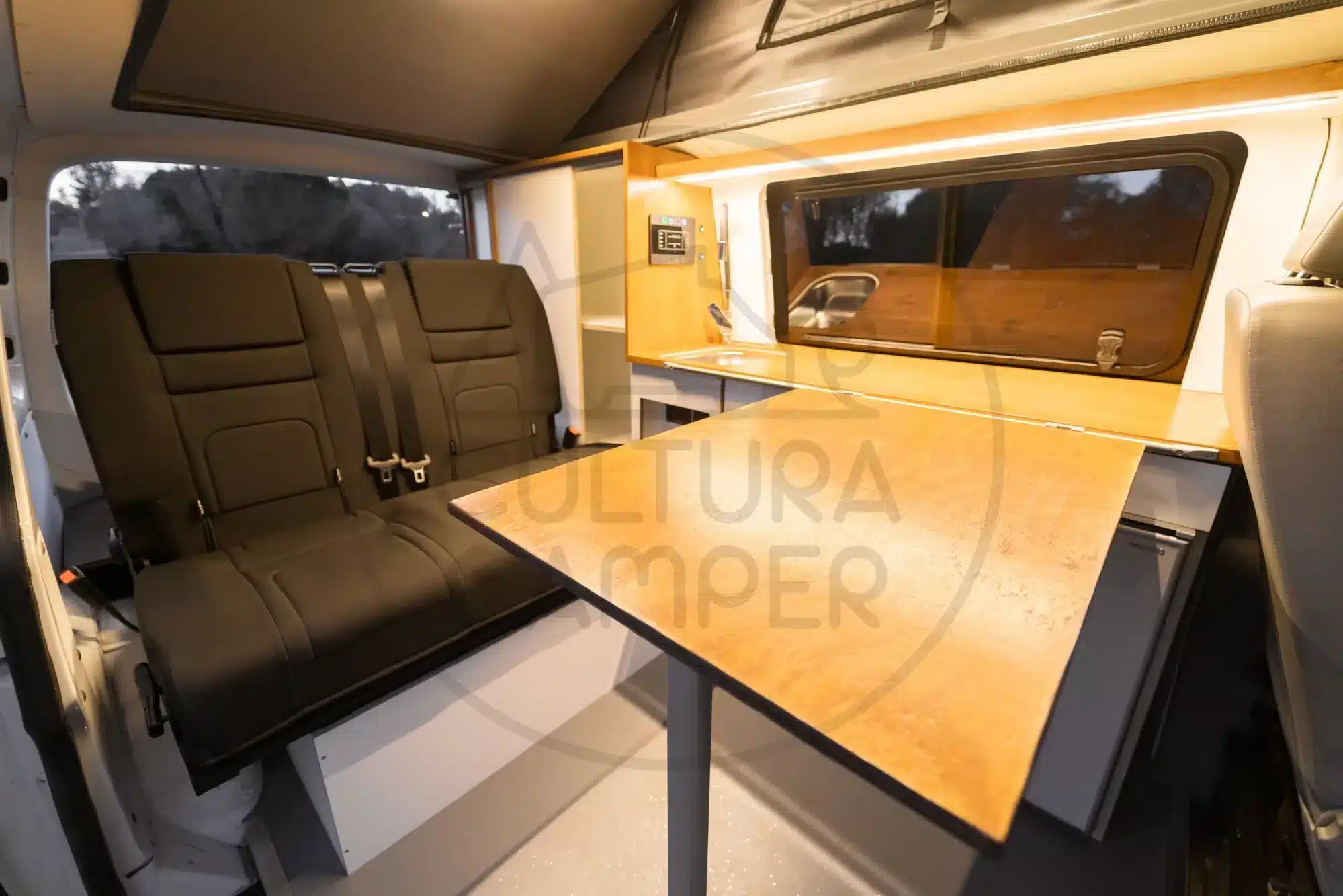 Innenraum eines Volkswagen T6 Campers mit Aufstelldach, Sitzbank, Tisch und Küchenzeile, ausgebaut in Spanien