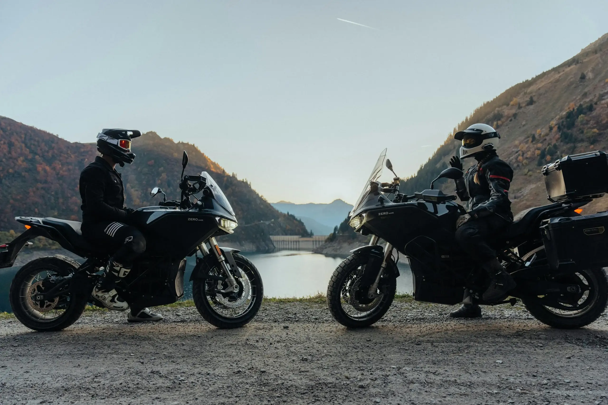Zwei Zero DSR/X Elektromotorräder mit Fahrern nebeneinander vor einem See und Bergen