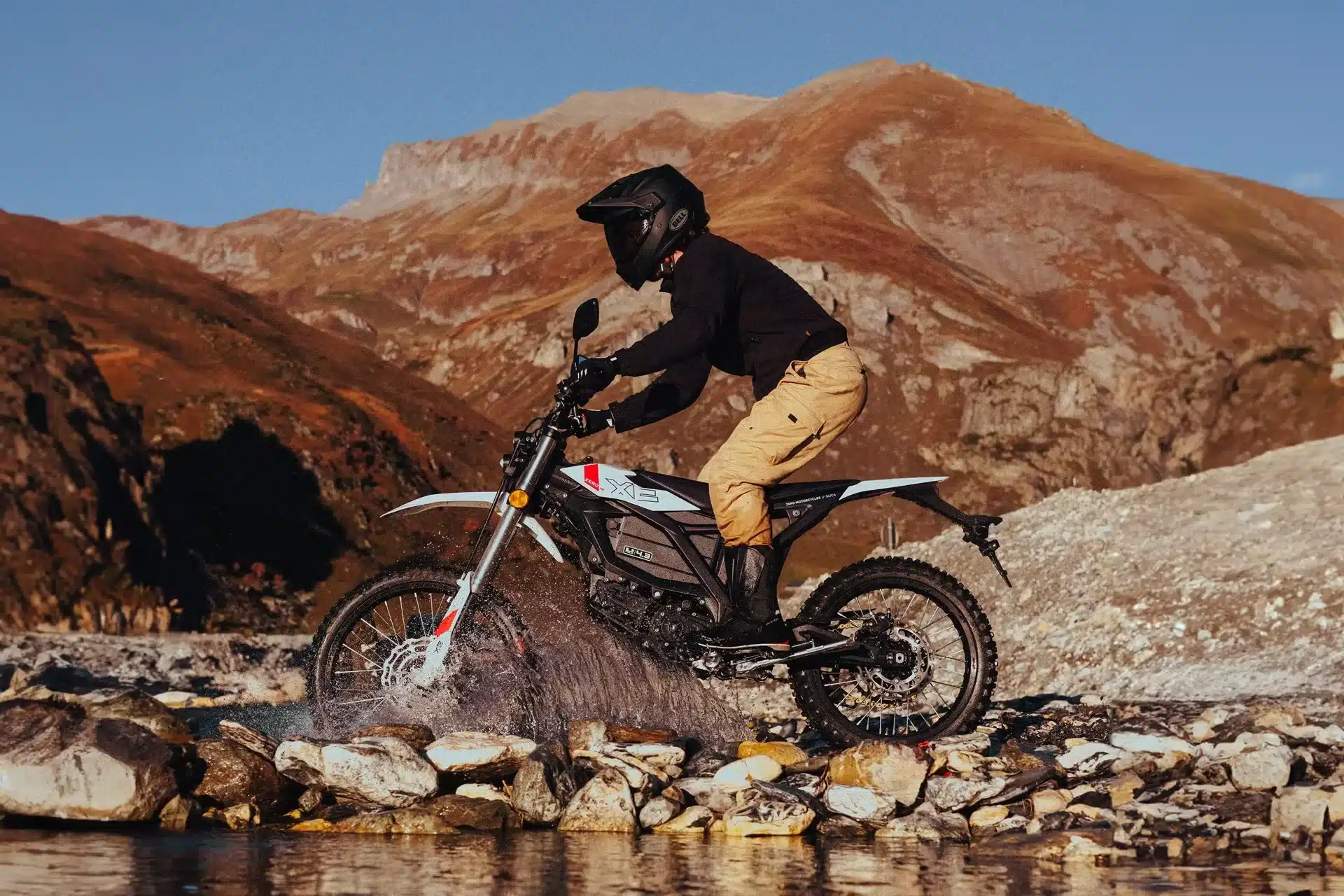 Fahrer mit Zero XE Elektro-Offroad-Motorrad überquert einen Bach im Gebirge.